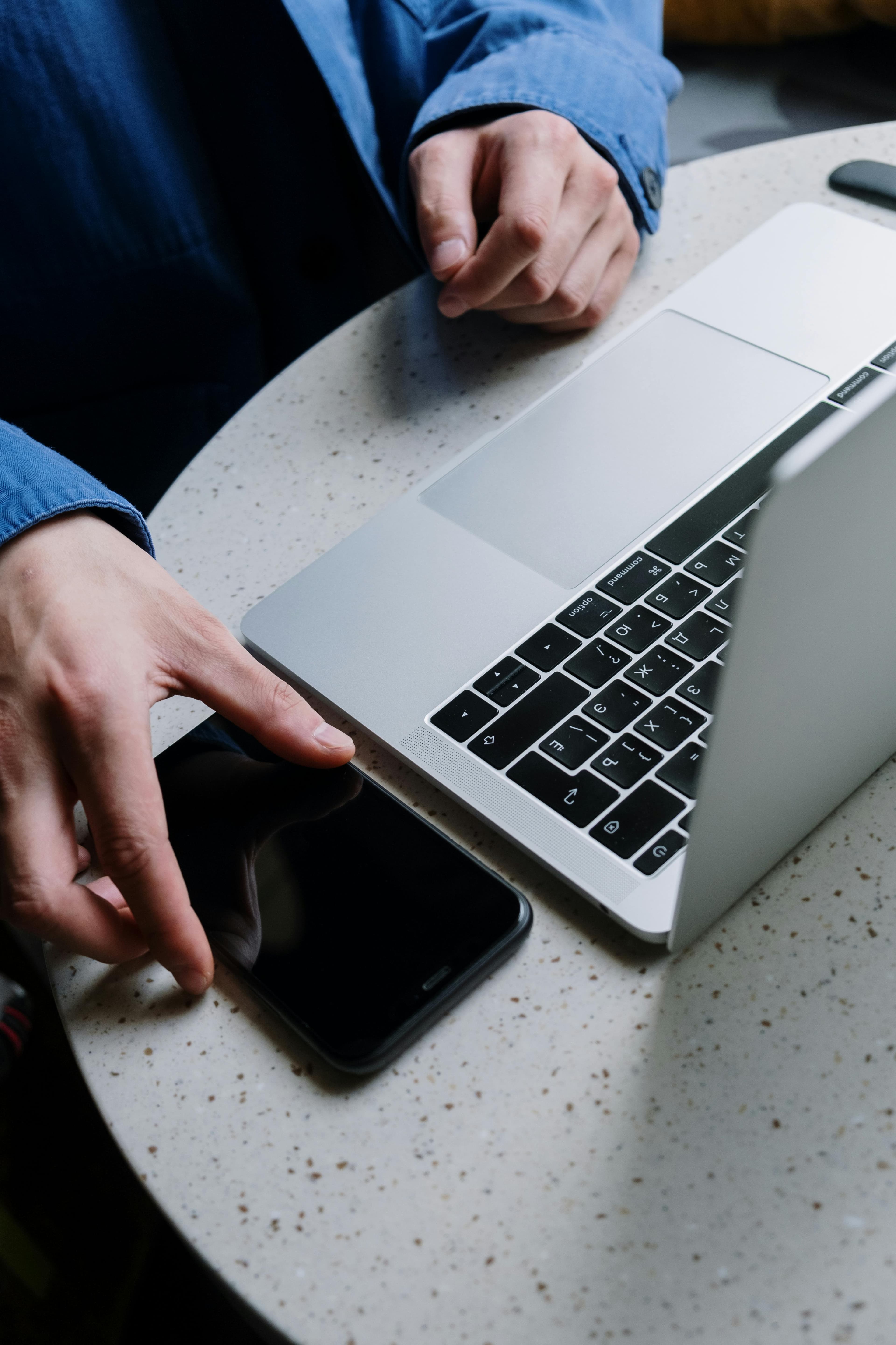 A person reaching for their phone next to a laptop on a café table.
