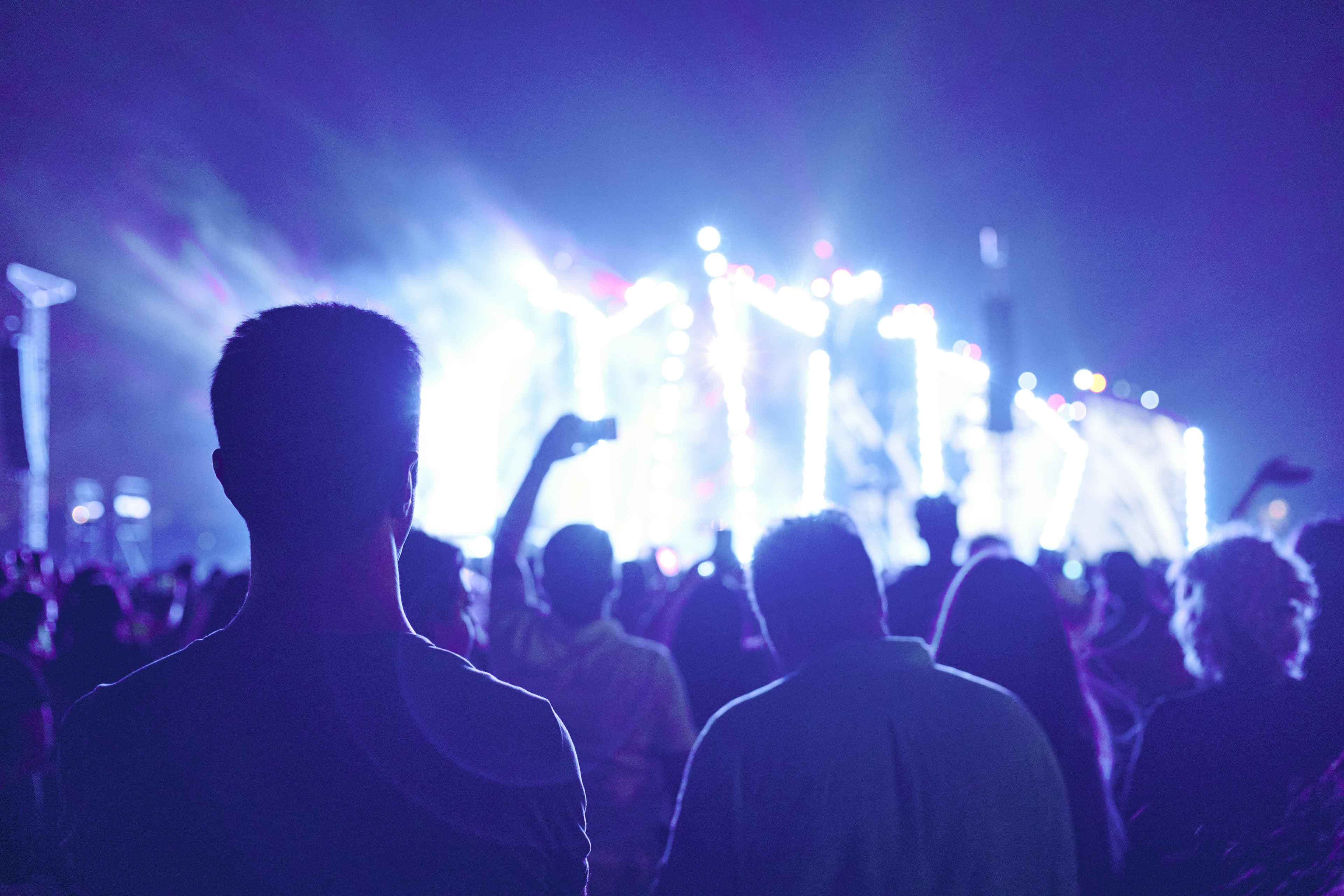Concert crowd silhouetted against a brightly lit main stage.